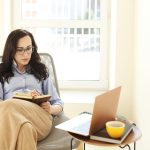 Adult businesswoman with laptop writing in notepad